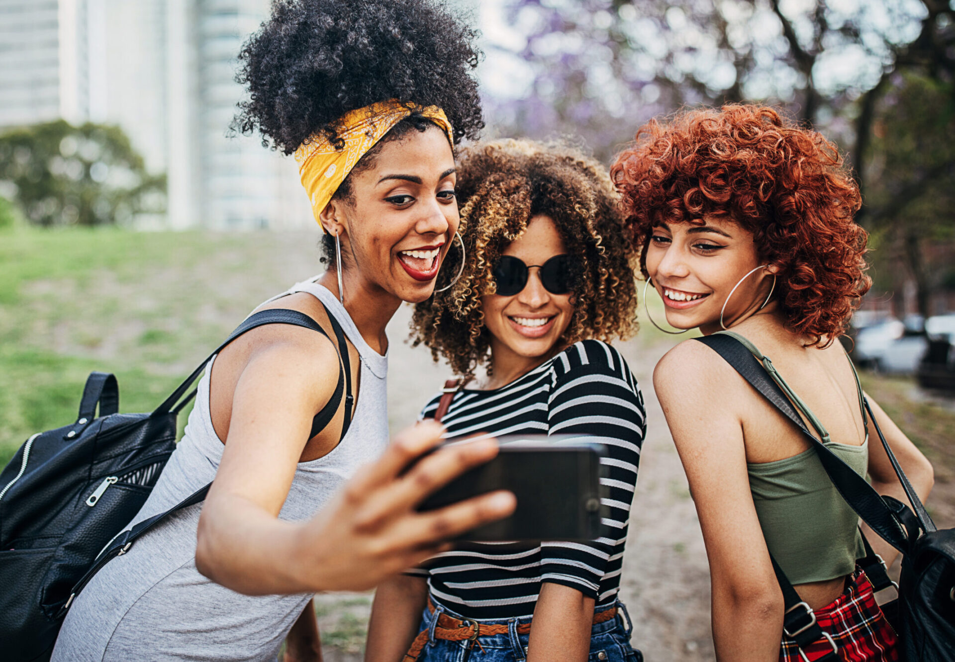 Three happy young women, smiling and taking a selfie outside.